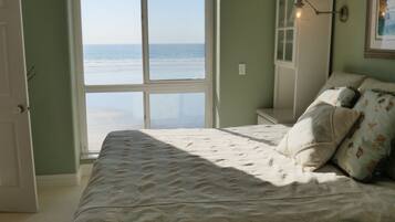 A bedroom with a bed, a ceiling fan, a view of the beach, and a door leading to the beach.