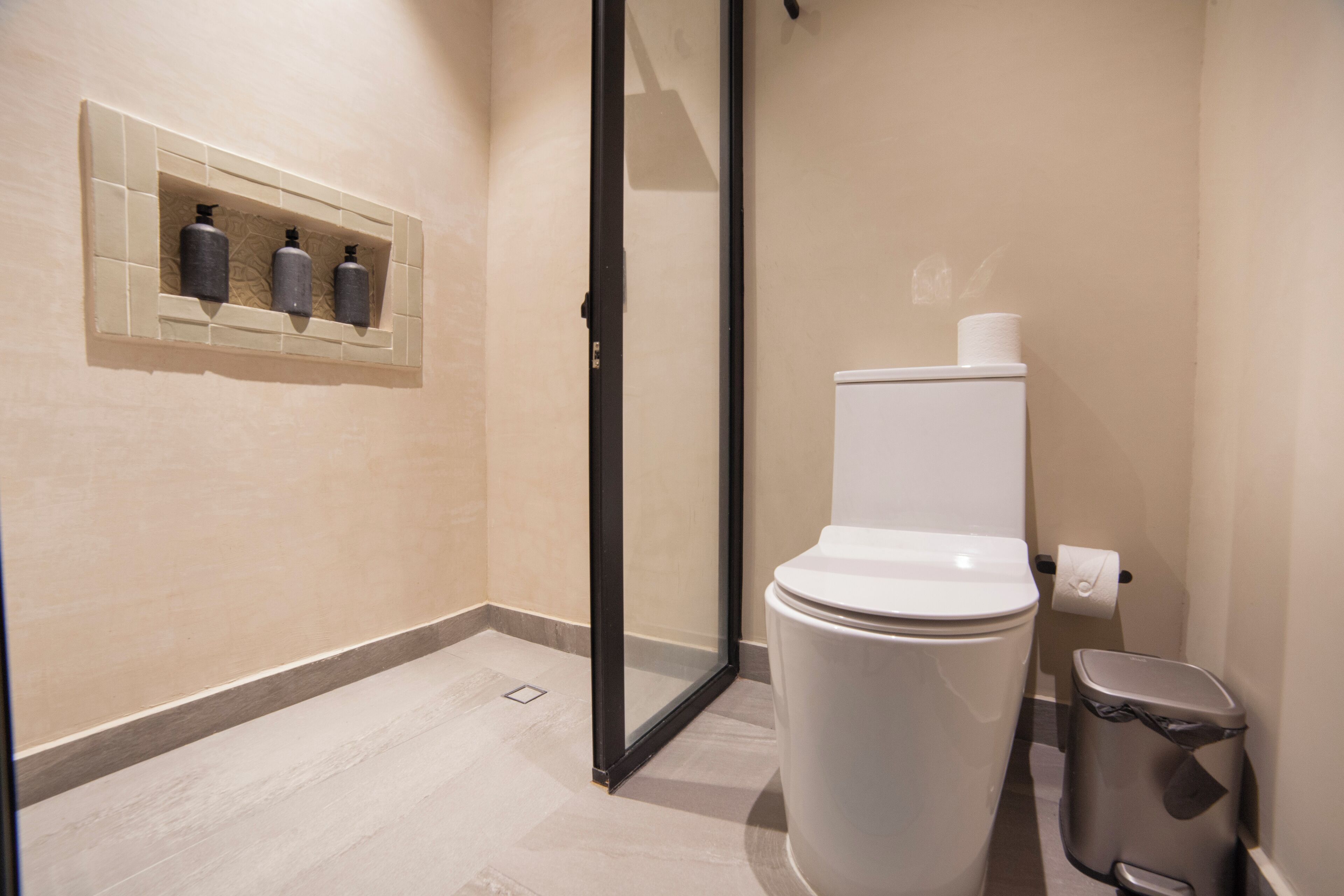 A modern bathroom with a toilet, a trash bin, and a shower area.