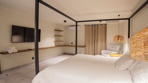A modern bedroom with a four-poster bed, a flat-screen TV mounted on the wall, a chair, and a small shelf with towels.