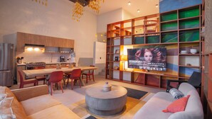 A modern living room with a sofa, coffee table, and TV. There is a kitchen area with cabinets and a dining table.