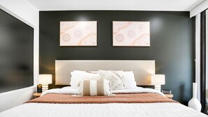 A modern bedroom with a large bed, two bedside tables, and two wall-mounted lamps. - Luxury Studio in Palm Cove Resort | Steps to Beach & Pools (Palm Cove)