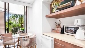 A modern kitchen with a dining area, featuring wicker chairs, a round table, a microwave, and a coffee maker. - Luxury Studio in Palm Cove Resort | Steps to Beach & Pools (Palm Cove)