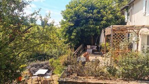 A garden with a stone wall, a table with chairs, and a wooden pergola. - Charming self-catering cottage in a Plus Beau Village, near Pompadour. (Ségur-le-Château)