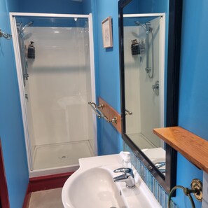 A bathroom with a glass-enclosed shower, a white sink, and a mirror with a wooden shelf.