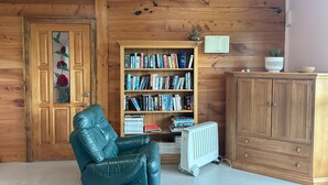 A cozy room with a leather recliner, a wooden bookshelf filled with books, a radiator, and a wooden cabinet. - Lavender Cottage at Akaroa Lavender (Duvauchelle)