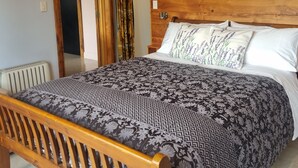 A bedroom with a wooden headboard, a bed with patterned bedding, a door with curtains, and a framed picture on the wall. - Lavender Cottage at Akaroa Lavender (Duvauchelle)
