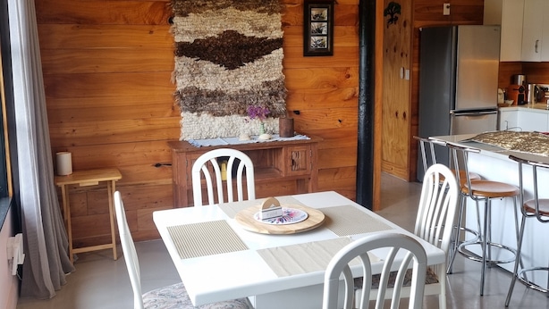 A wooden interior with a dining area, kitchen, and a wall-mounted rug. - Lavender Cottage at Akaroa Lavender (Duvauchelle)