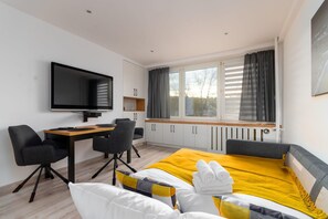 A modern hotel room with a bed, a desk, a chair, a television, and a window with curtains. - Plac Grunwaldzki Inviting Apartment (Wrocław)