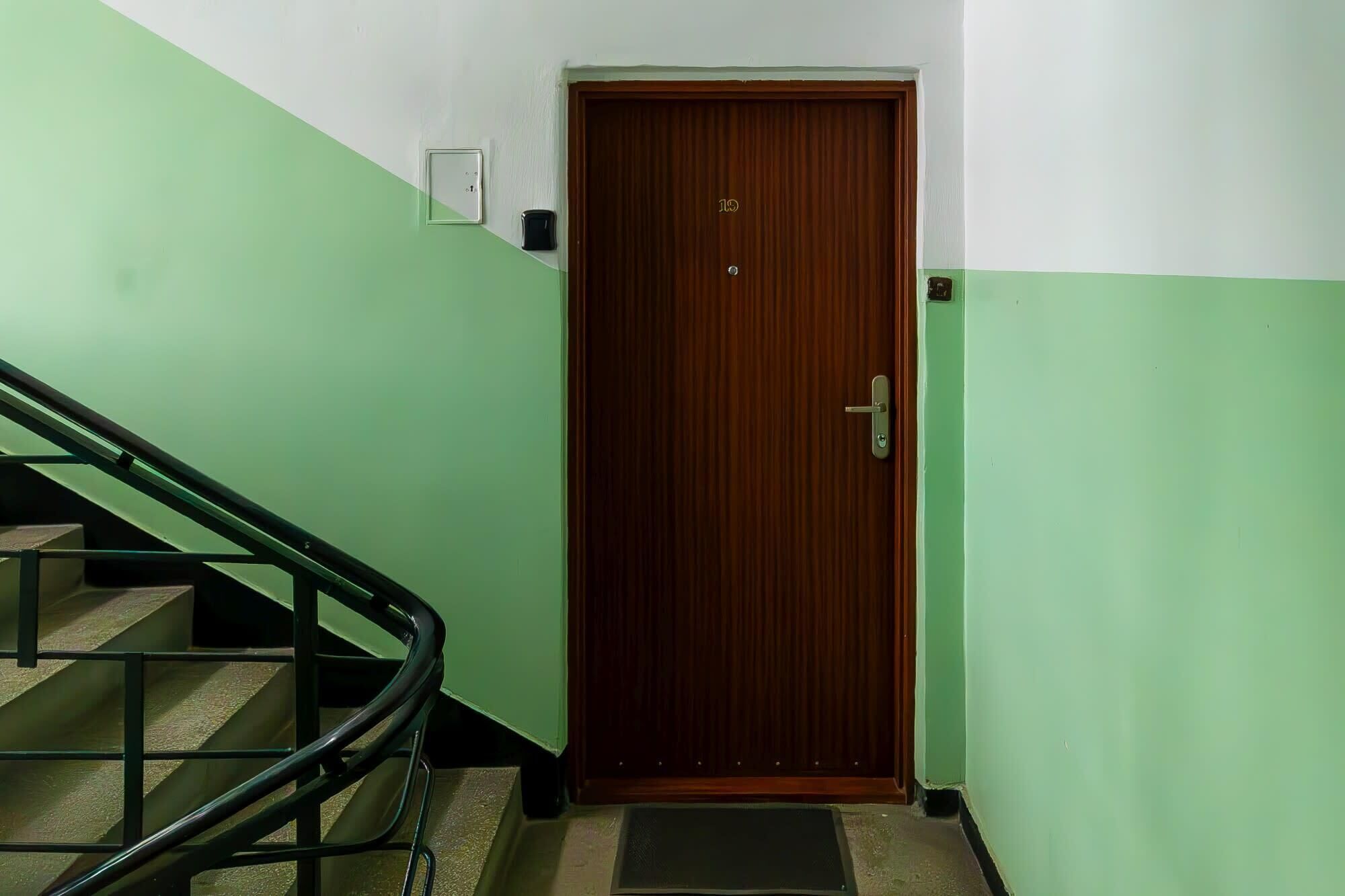 Une porte en bois avec une plaque portant un numéro, une main courante en métal et un mur aux couleurs verte et blanche.