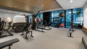 Ein modernes Fitnessstudio mit unterschiedlichen Trainingsgeräten, einem Gewichtständer und einem großen Fenster mit Blick ins Freie.