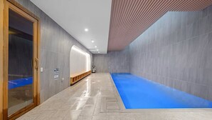 Ein moderner, überdachter Swimmingpool mit blauer Wasseroberfläche, einer hölzernen Sitzbank an einer Wand und einem gefliesten Boden.