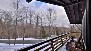 Una terraza de madera con un banco, con vistas a un paisaje nevado con árboles y una carretera.