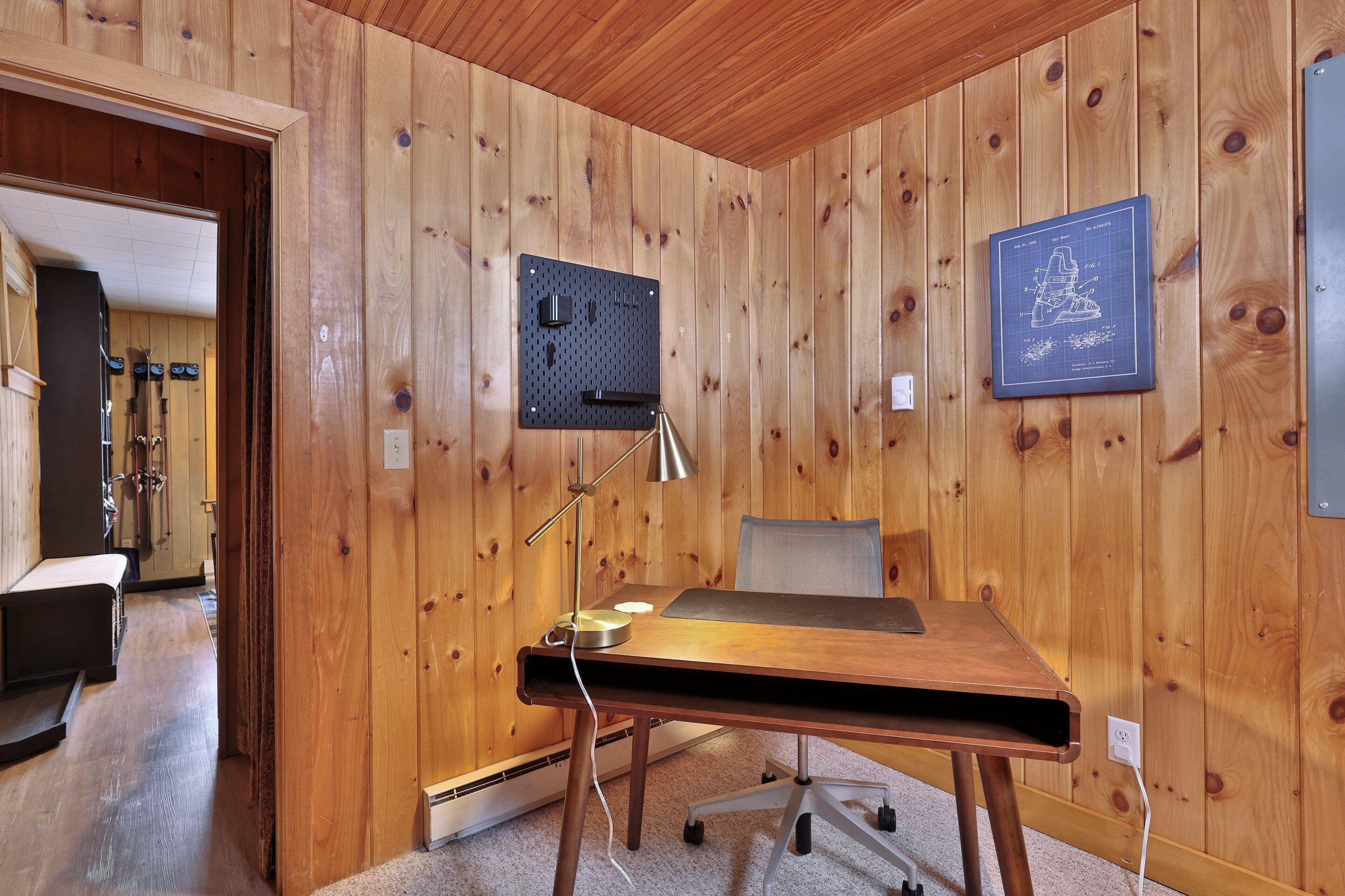 A wooden-paneled room with a desk, a pegboard, and a framed blueprint on the wall.