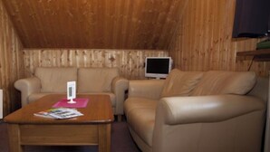 Una habitación acogedora con techo de madera, un sofá color beige, un sillón de cuero y una pequeña mesa de madera con una revista.