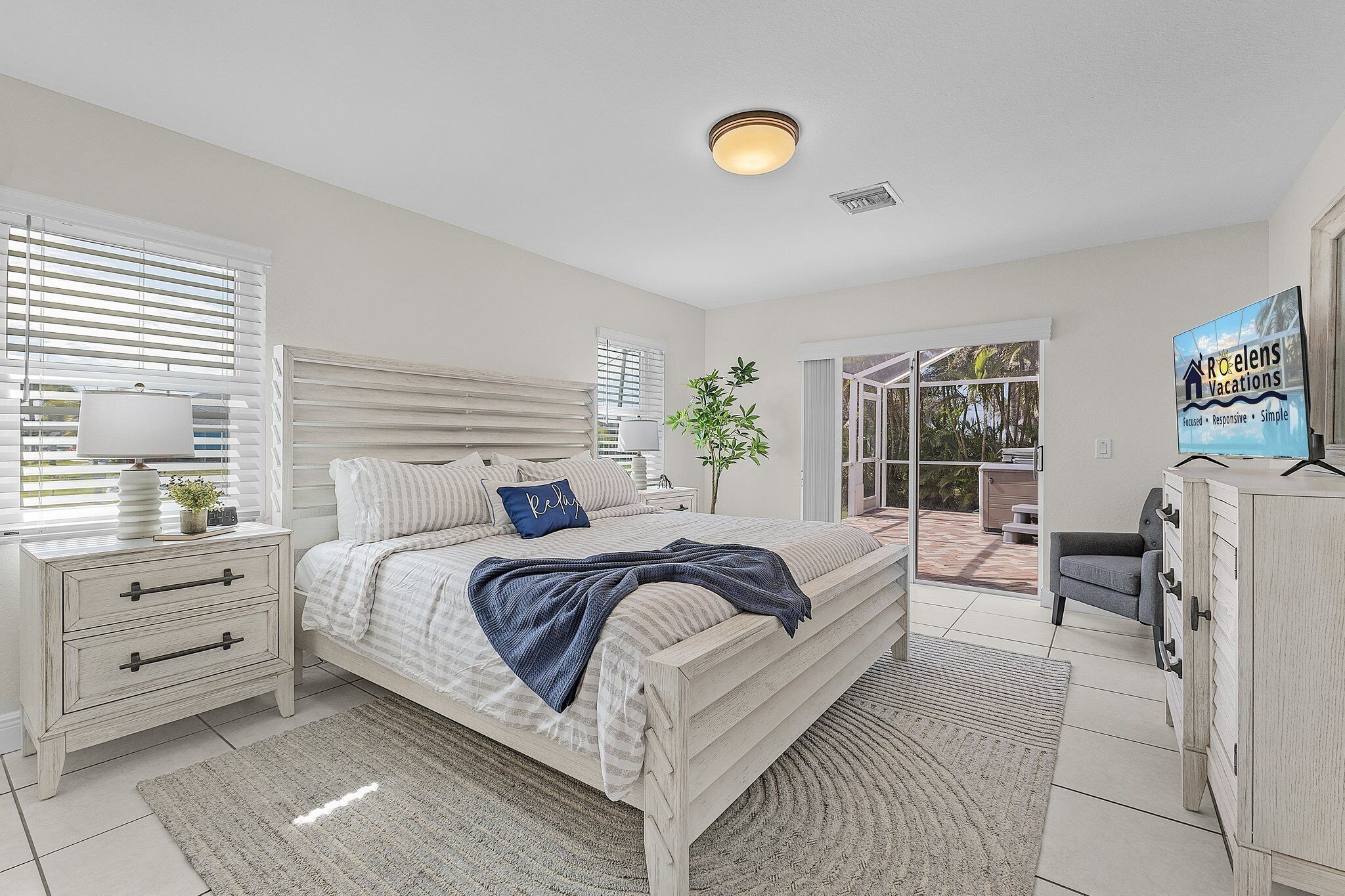 A bedroom with a bed, bedside tables, a nightstand, a dresser, a potted plant, and a view of the outdoors.