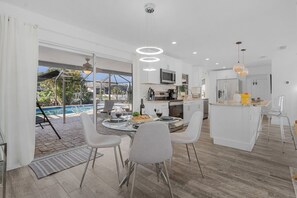 Una cocina moderna con comedor, vista a la piscina y una pequeña isla con taburetes de bar.
