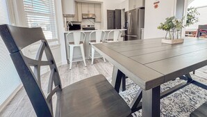A modern kitchen with white cabinets, a stainless steel refrigerator, and a dining area with a wooden table and chairs. - Spacious and conveniently located 5 Bedroom 3 Bath home in SLC with Amenities (Salt Lake City)