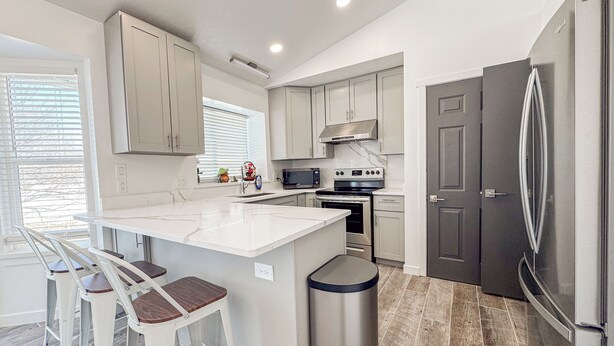 A modern kitchen with a central island, stainless steel appliances, and a grey refrigerator. - Spacious and conveniently located 5 Bedroom 3 Bath home in SLC with Amenities (Salt Lake City)