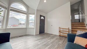 A spacious living room with a high ceiling, large windows, a dark door, and a staircase. - Spacious and conveniently located 5 Bedroom 3 Bath home in SLC with Amenities (Salt Lake City)
