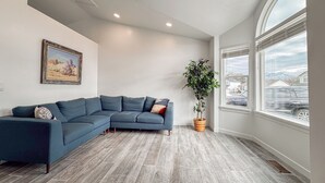 A modern living room with a sectional sofa, a large window with a view of houses, and a potted plant. - Spacious and conveniently located 5 Bedroom 3 Bath home in SLC with Amenities (Salt Lake City)