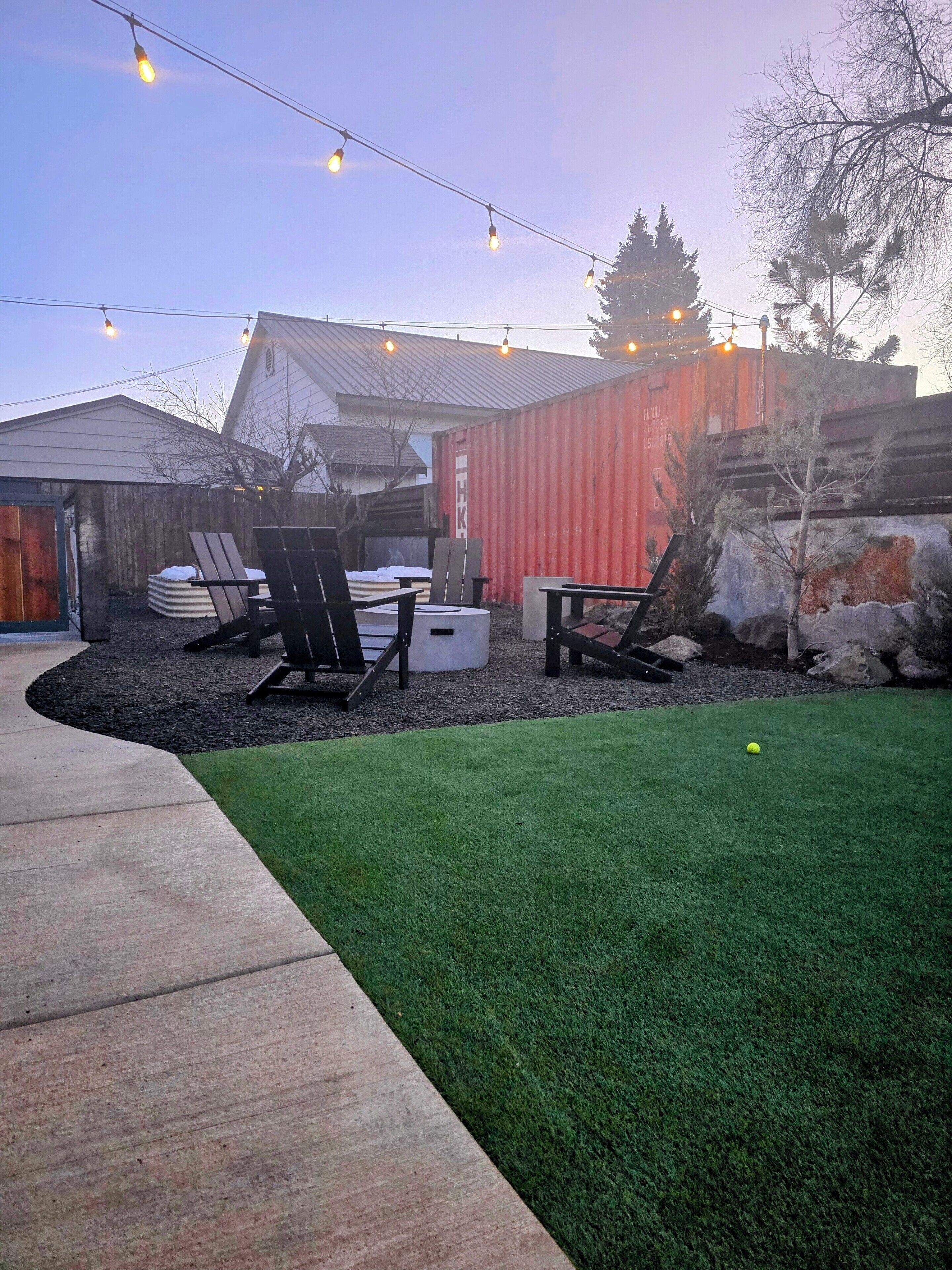 A backyard with artificial lighting, outdoor furniture, and a green lawn.