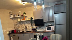 A modern kitchen with a dining area, featuring a wooden table, grey upholstered chairs, and stainless steel appliances.