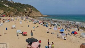 A crowded beach with numerous umbrellas and beachgoers.