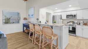 A modern kitchen with white cabinets, a central island with bar stools, a microwave, a refrigerator, and an oven.