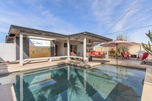 Un área junto a la piscina con un porche cubierto, mobiliario exterior y un jardín de cactus.