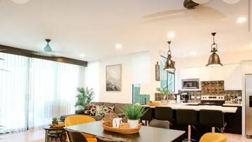 Una cocina moderna con una isla central, iluminación colgante y un comedor con mesa y sillas.