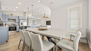 A modern kitchen with a central island, stainless steel appliances, and a dining area with a large table and chairs. - The Blue Buffalo: Private Pool, Resort Amenities (Corolla)