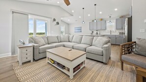 A spacious living room with a large L-shaped grey sofa, a wooden coffee table, and a ceiling fan. - The Blue Buffalo: Private Pool, Resort Amenities (Corolla)