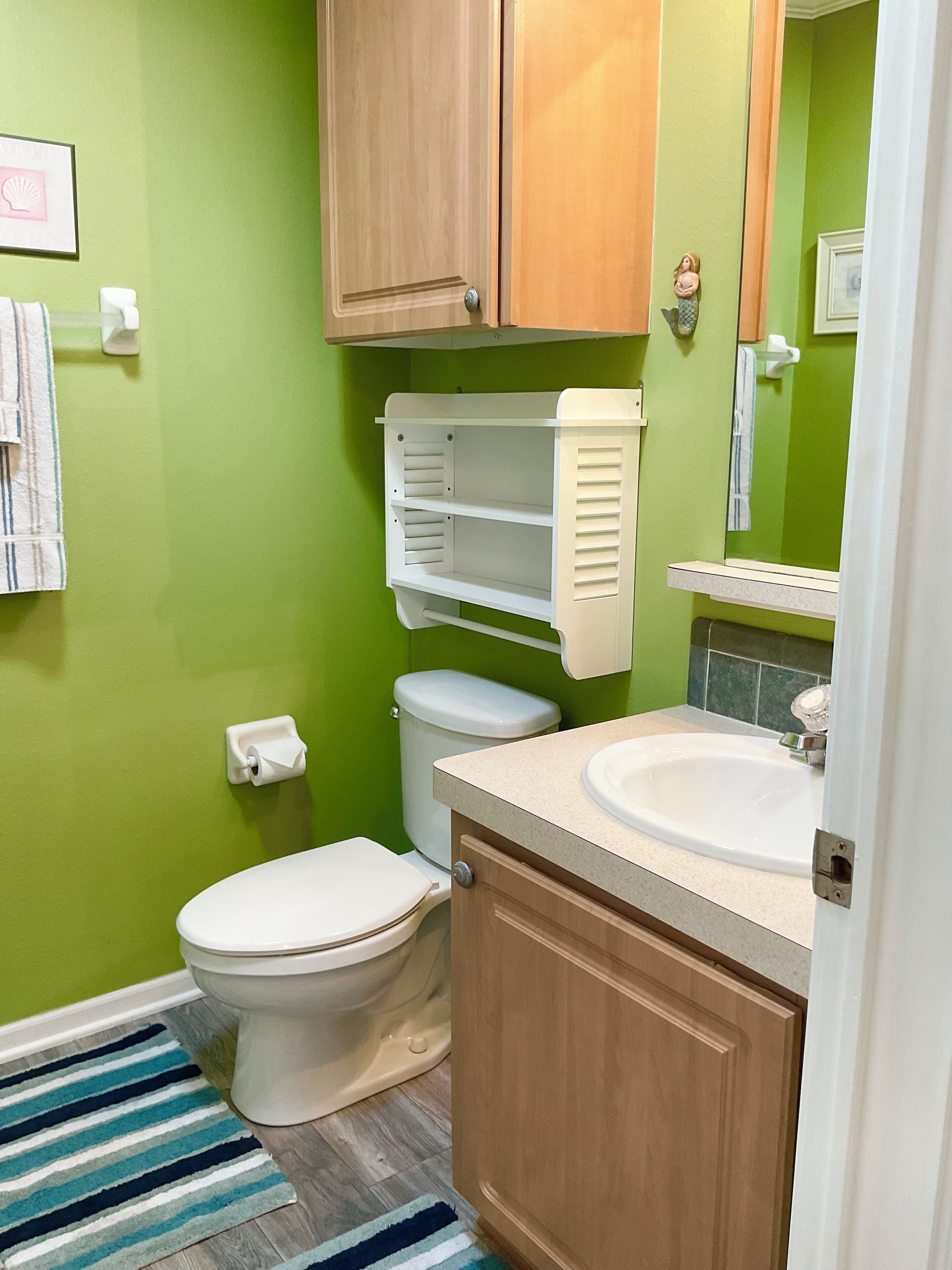 A bathroom with a green wall, a white toilet, a sink, and a mirror.