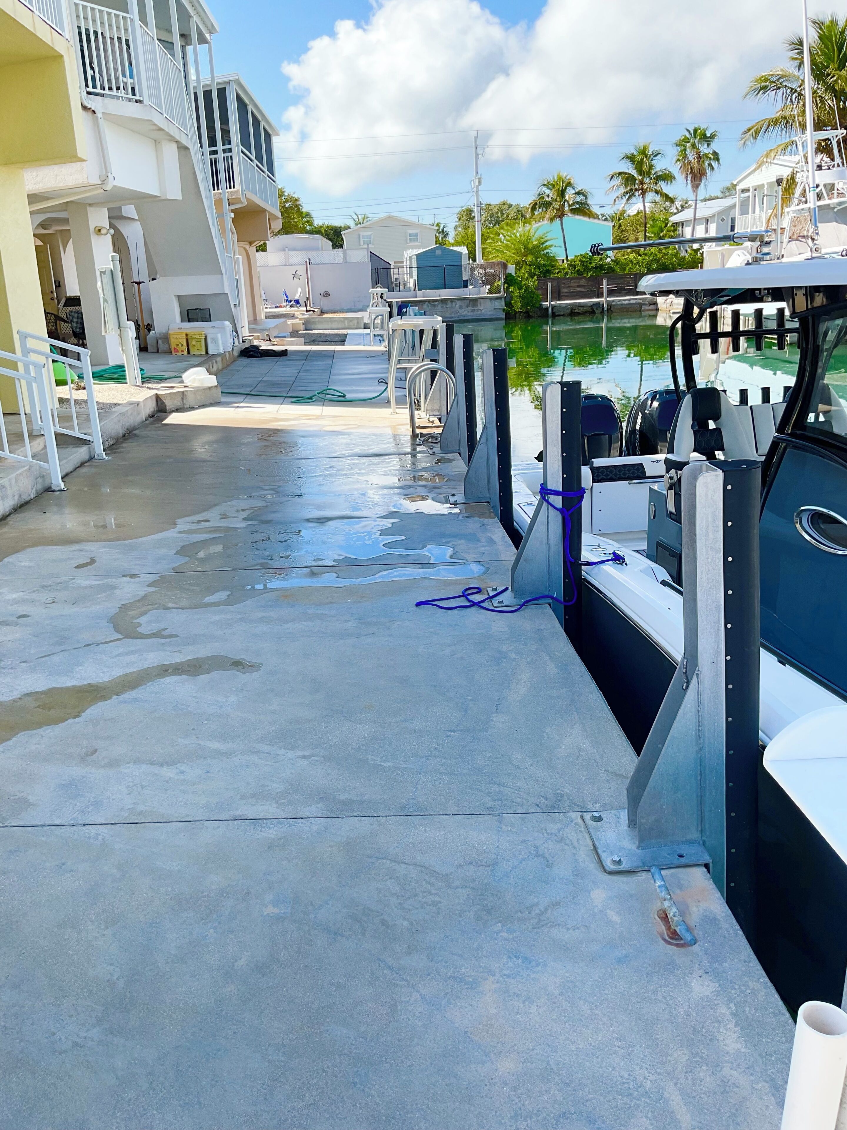 A marina with boats docked, a concrete walkway, and a building with balconies.