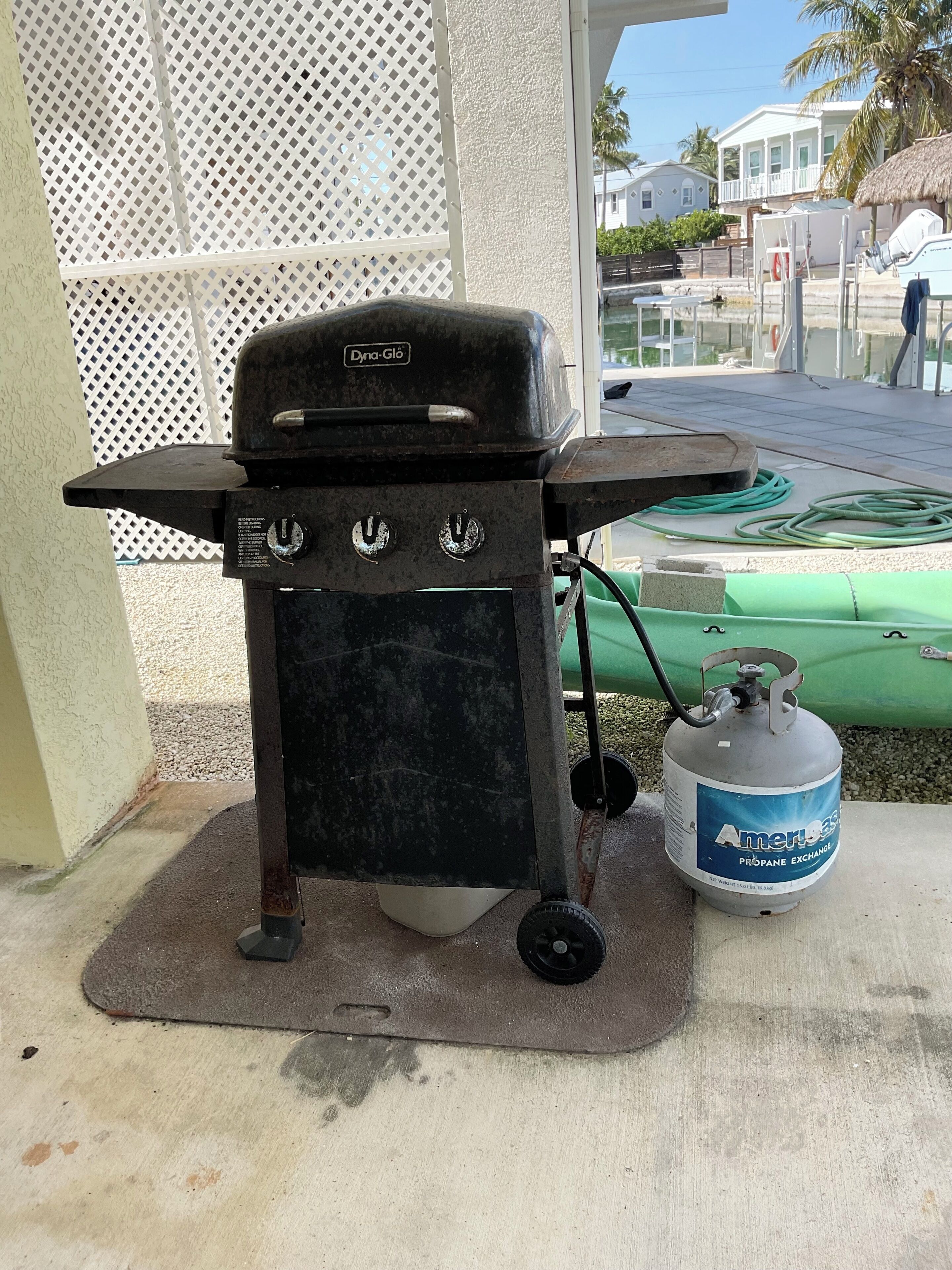 A portable grill with a propane tank, placed on a concrete surface outdoors.