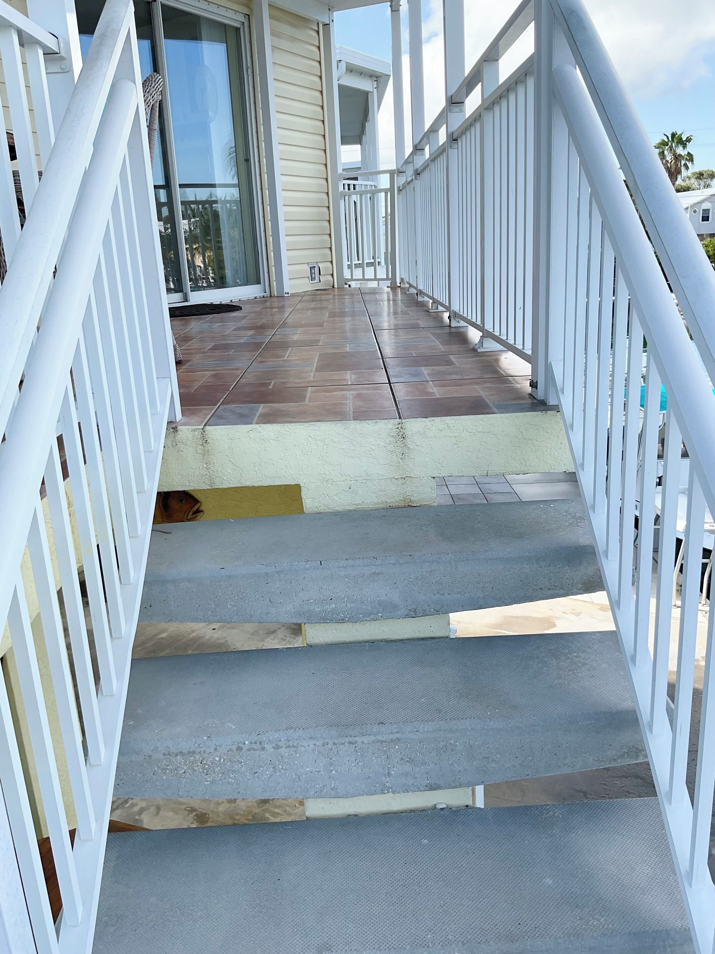 Una escalera con barandillas blancas que conduce a un espacio exterior cubierto con piso de baldosas.