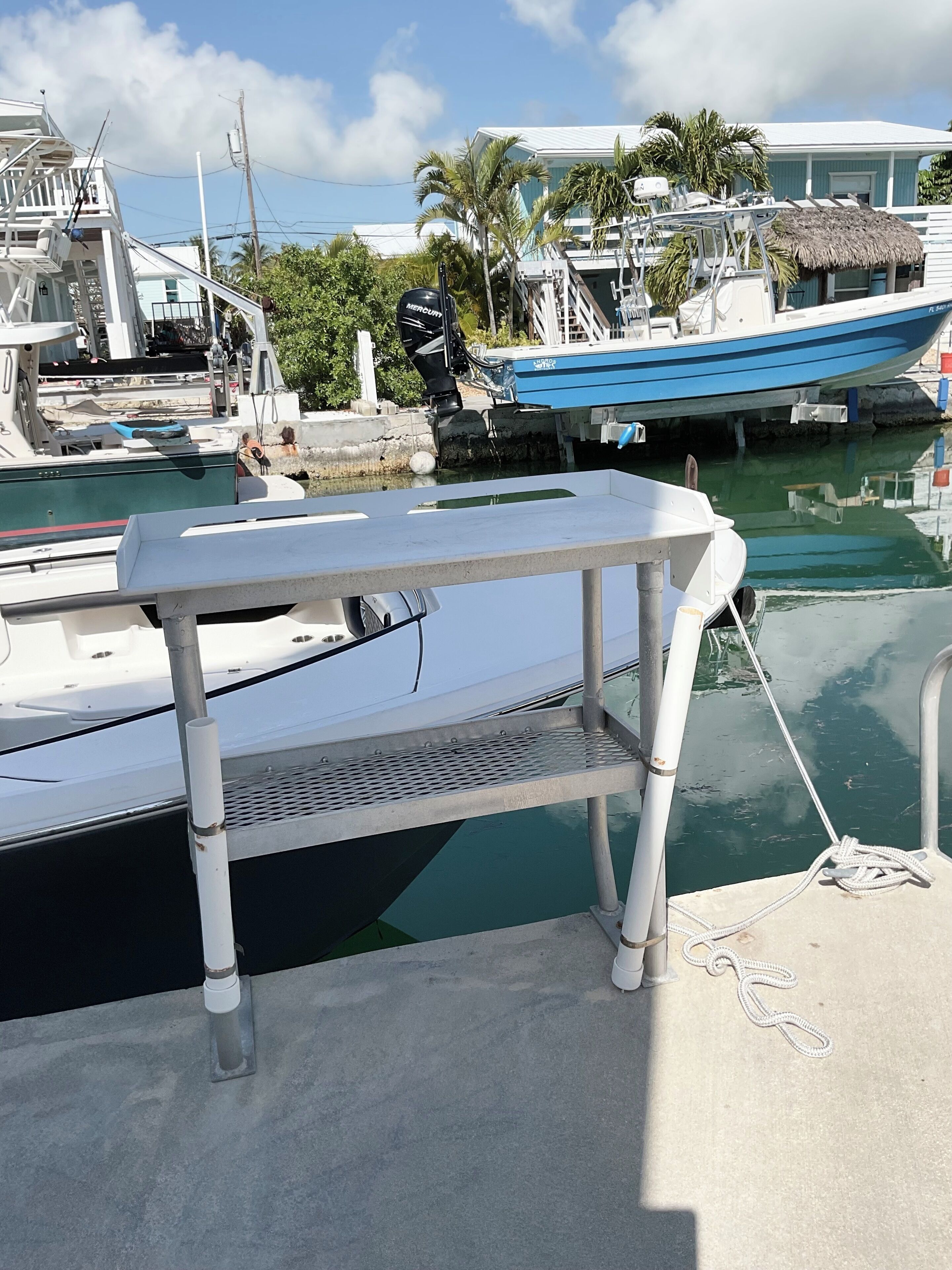 Ein Yachthafen mit vor Anker liegenden Booten, ein weißes Boot mit einem Mercury Außenmotor und einem Reetdachgebäude.
