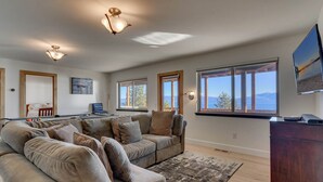 A spacious living room with a large sectional sofa, a pool table, and a view of the ocean through large windows.