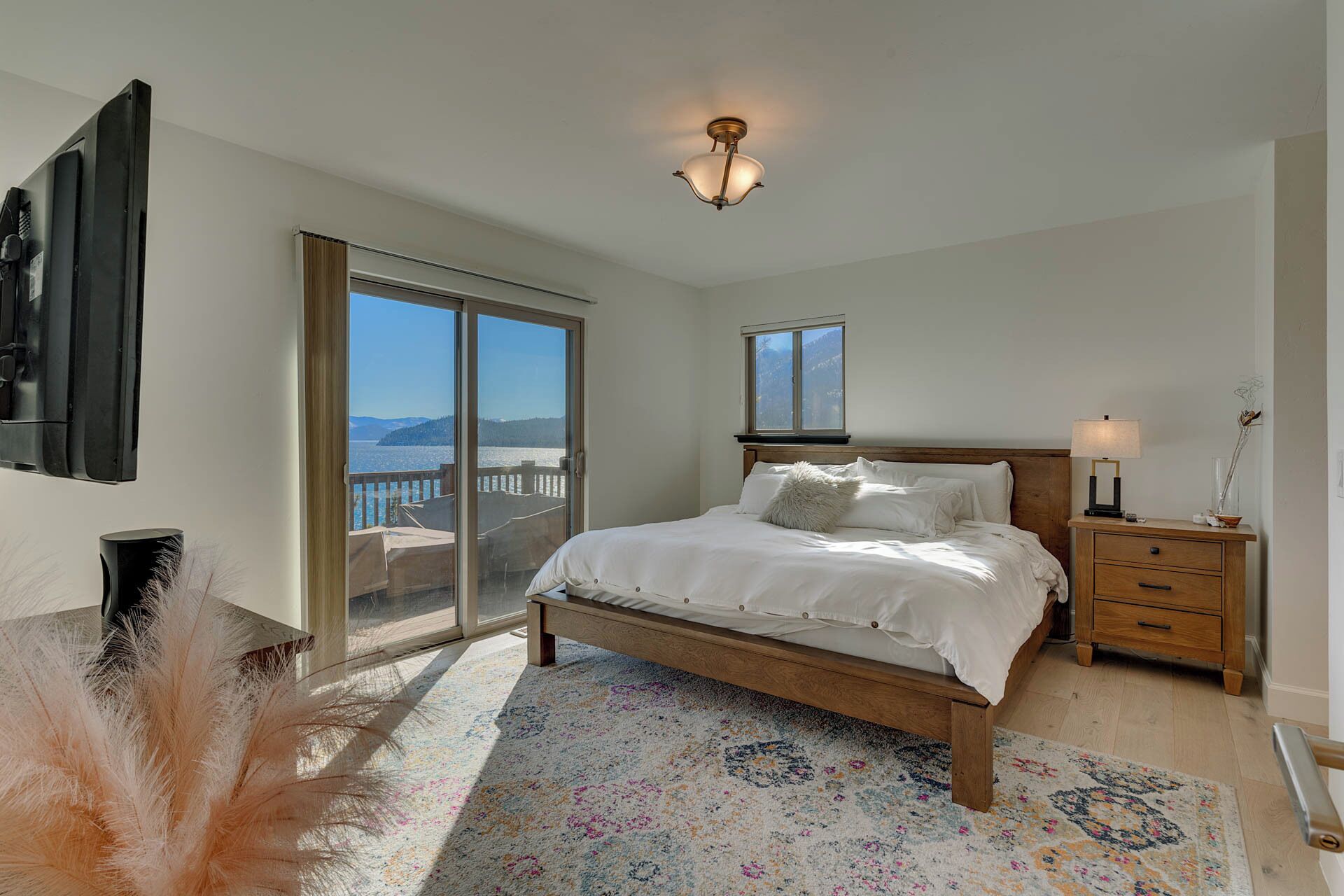 A bedroom with a bed, a nightstand, a lamp, a dresser, a sliding glass door, and a view of the outdoors.