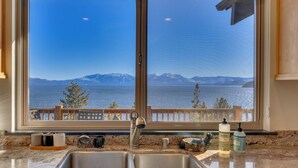 A kitchen with a large window overlooking a lake and mountains.