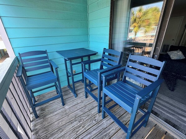 A porch with a blue table and chairs, wooden flooring, and a view of the outside.