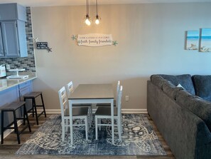 Een moderne woonkamer met een eethoek, een grijze bank, een vloerkleed met dessin en een keuken met blauwe kastjes.