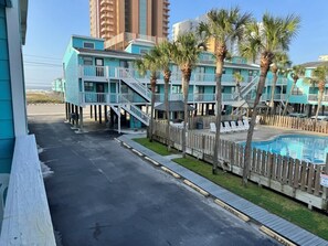 A beachfront hotel with multiple blue buildings, a wooden deck, a pool, and palm trees.