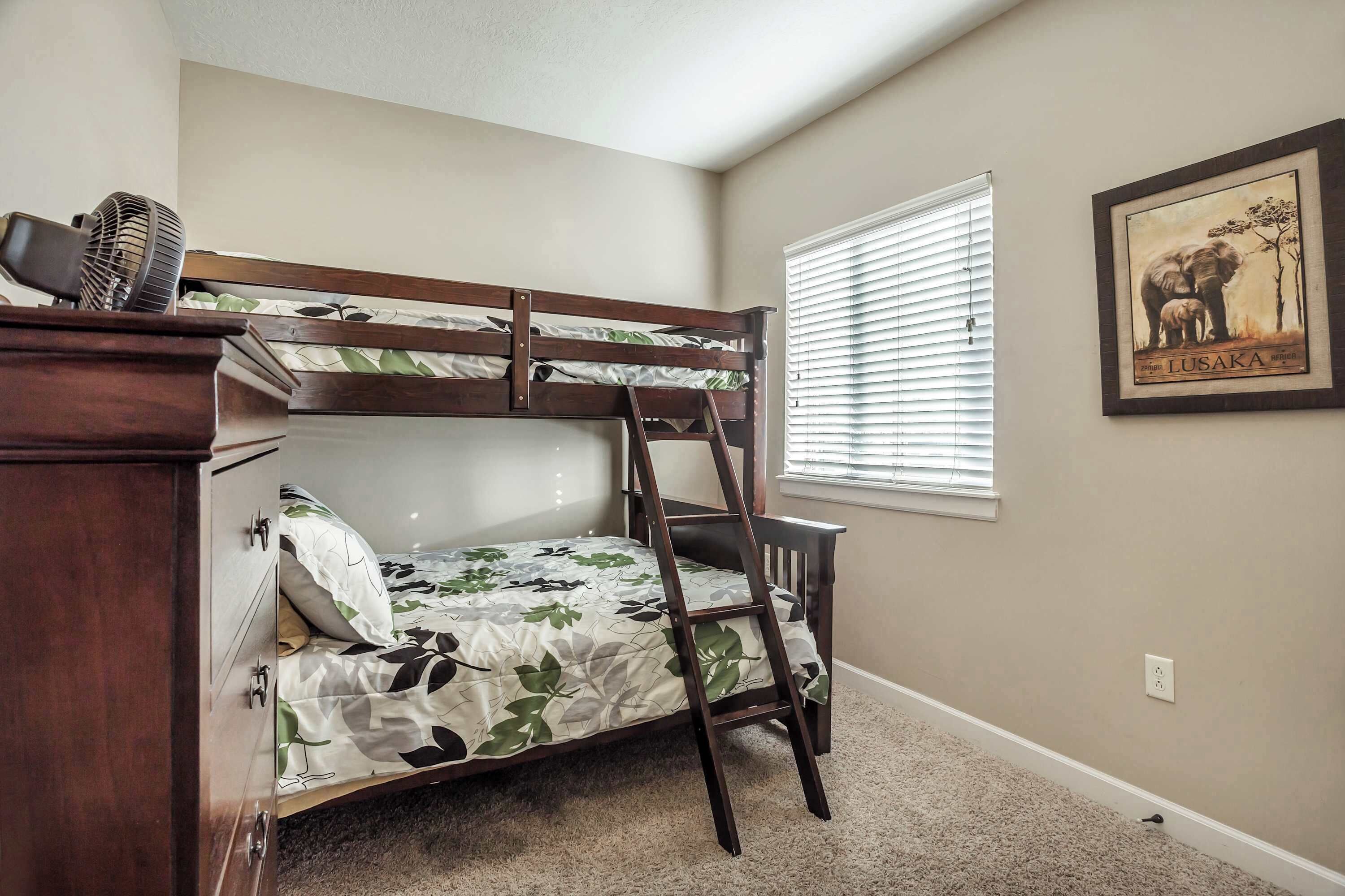 A bunk bed with a ladder, a desk, and a window with blinds.