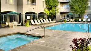 Une piscine entourée de chaises longues et de parasols, elle-même bordée d’un bâtiment doté de balcons et d’arbres.