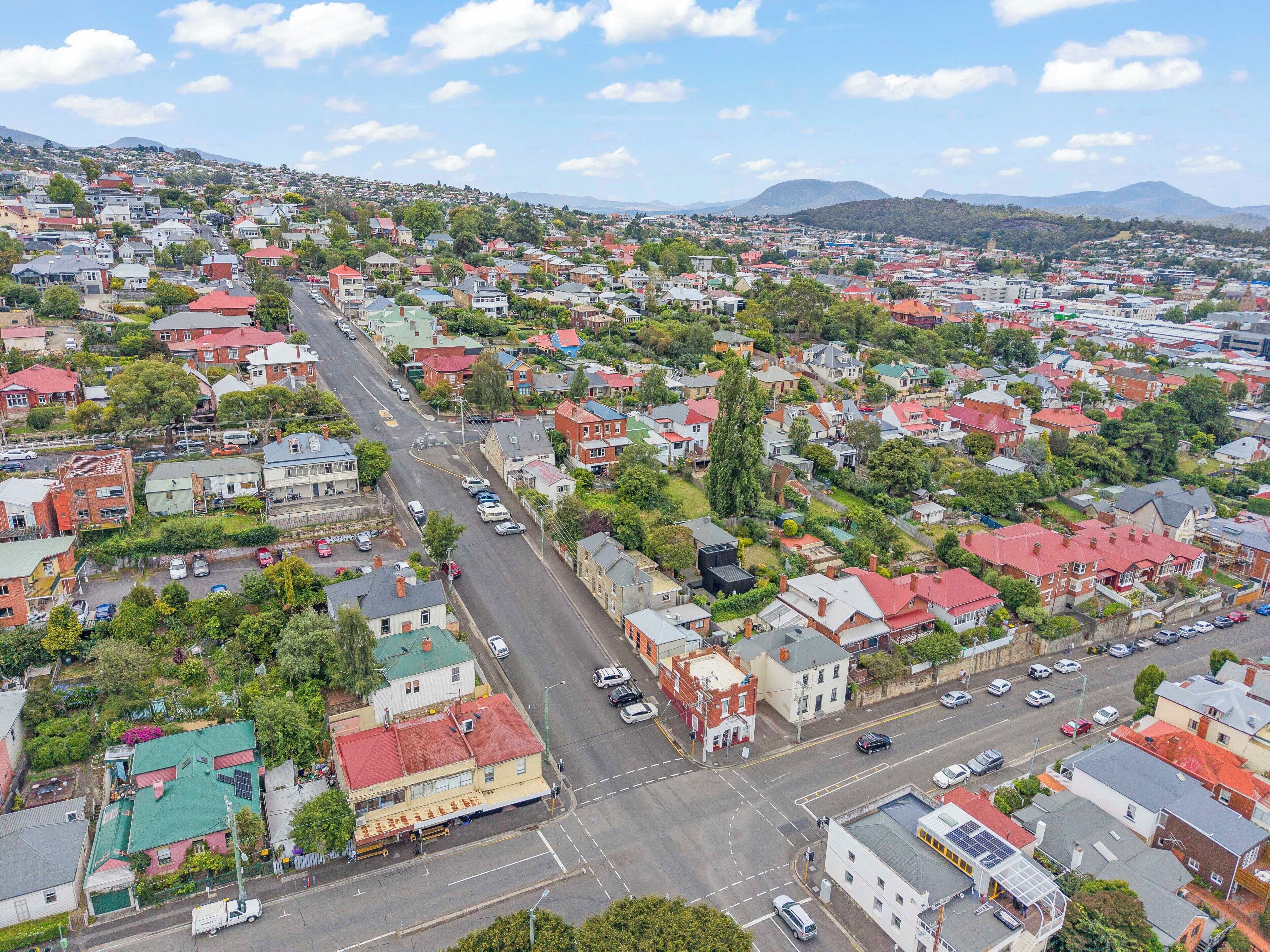An aerial view of a residential area with houses, streets, and a hilly landscape in the background.