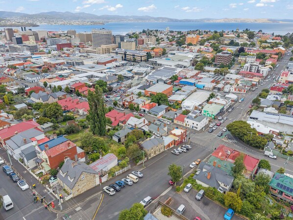 An aerial view of a cityscape with a mix of residential and commercial buildings, streets, and a distant view of the sea.
