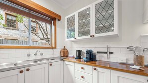 Una cucina con mobili bianchi, un piano di lavoro in legno, un fornello integrato e una finestra che si affaccia su un muro di pietra e alberi.