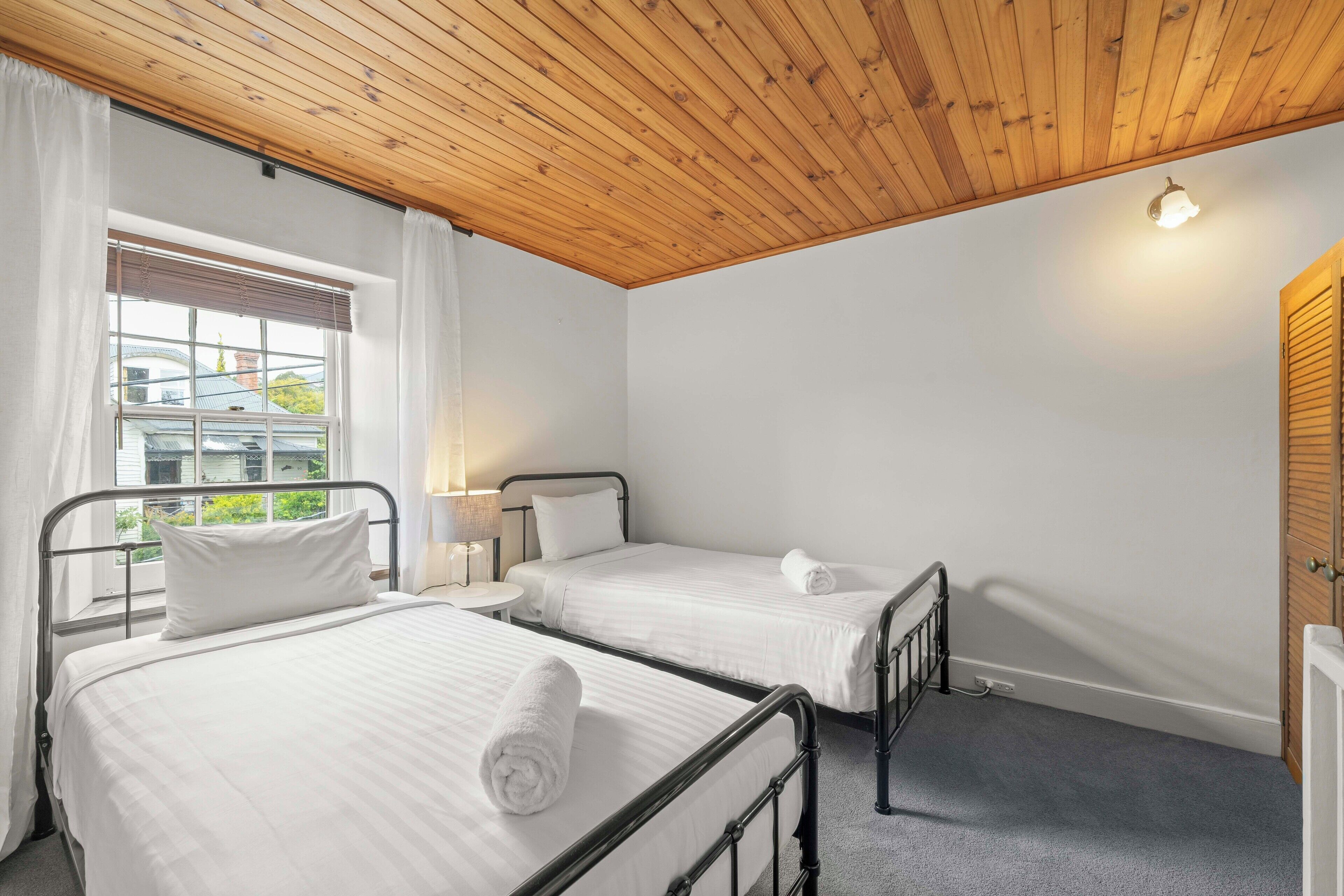 Een slaapkamer met twee bedden, een houten plafond, witte muren en een raam met gordijnen.
