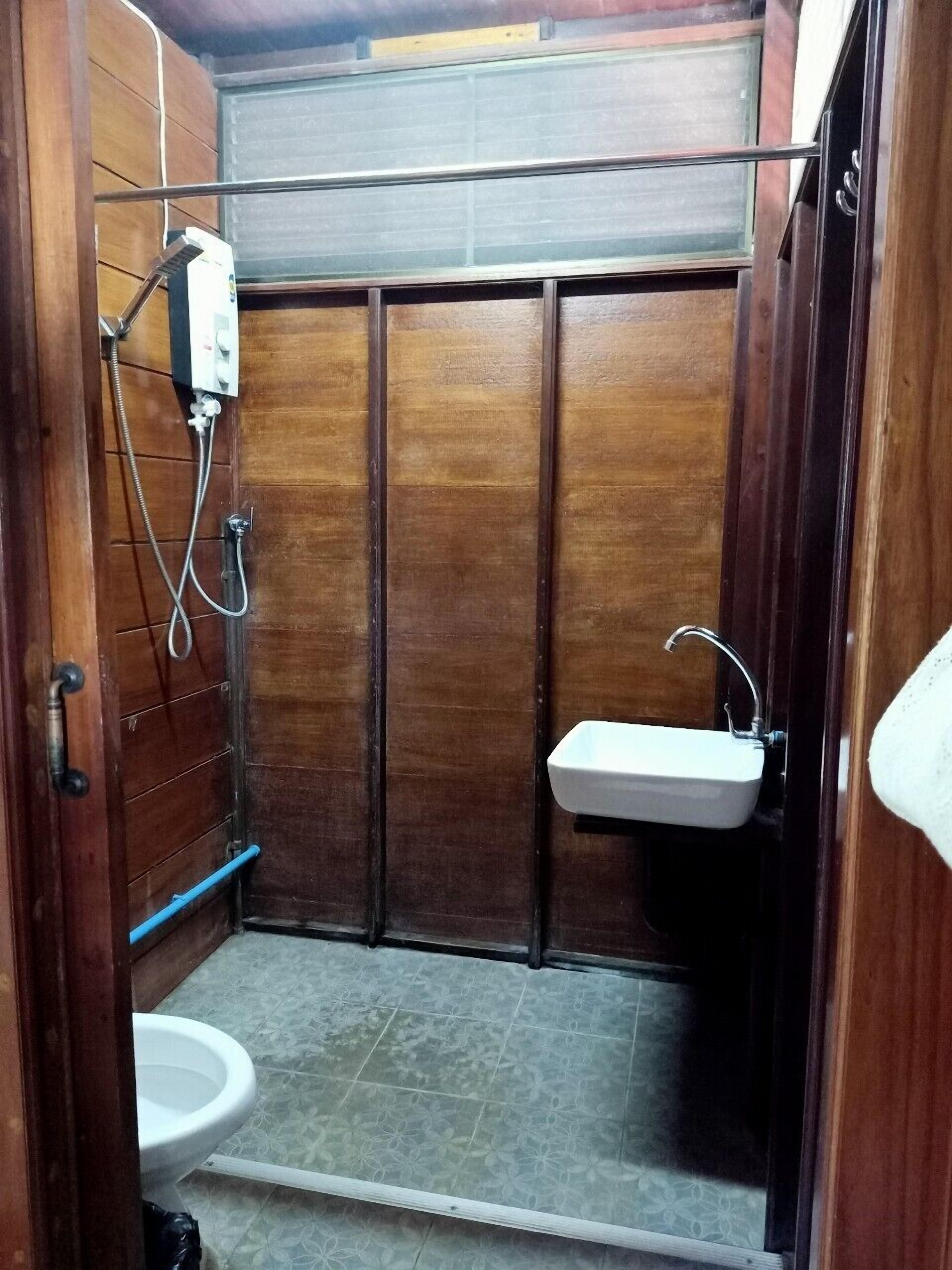 A small, enclosed bathroom with a wooden door, a toilet, a sink, and a shower.